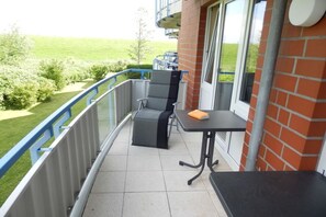 Un balcón con mesa y sillas, vistas a un paisaje verde y un muro de ladrillo.