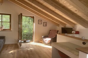 A room with a sloped ceiling, a sofa, a chair, a small table, and a window with a view of greenery. - Holiday apartment with 1 bedroom (Schönau am Königssee)