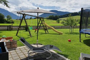 Ein Garten mit Schaukel, Rutsche, Trampolin und einer Sitzgruppe mit Tisch und Stühlen.
