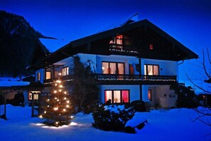 A two-story house with a balcony, surrounded by snow, and a decorated Christmas tree in front. - Holiday apartment with 2 bedrooms (Ruhpolding)