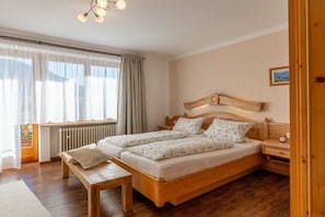 Ein Schlafzimmer mit einem Doppelbett, Nachttischen, einer Bank, einem Fenster mit Vorhängen und einem Heizkörper.