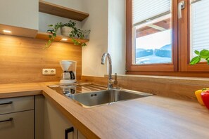 A kitchen with a stainless steel sink, wooden countertop, and a window with a view of a snowy landscape. - Holiday apartment with 2 bedrooms (Ruhpolding)