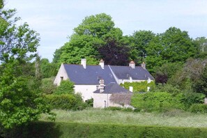 A house with a sloped roof, surrounded by dense greenery and trees. - Holiday apartment with 2 bedrooms (Ste. Honorine des Pertes)