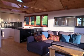 A modern kitchen with a central island, a dining area with a sofa and chairs, and a large window with a view of the outdoors.