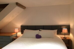 A bedroom with a bed, two bedside lamps, a wooden nightstand, and a sloped ceiling.