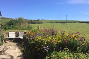 A stone pathway leading to a seating area with white chairs, surrounded by a variety of colorful flowers.