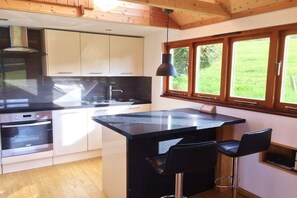 A modern kitchen with a central island, stainless steel appliances, and a window overlooking a green landscape.