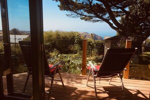 A wooden deck with two chairs and a table, overlooking a garden and distant hills.