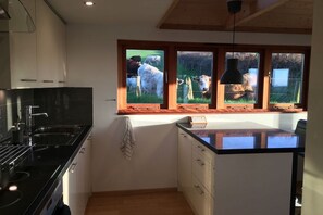 Una cocina con estufa negra, armarios blancos y ventana con vista a vacas.