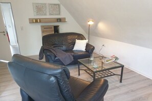A living room with a leather sofa, a glass coffee table, and a floor lamp. - Holiday apartment in Hage with swimming pool (Hage)