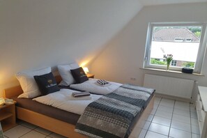 A bedroom with a bed, pillows, a bedside table, a window with a view, and a radiator. - Holiday apartment in Hage with swimming pool (Hage)