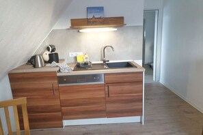 A compact kitchen with a built-in dishwasher, a stainless steel kettle, a coffee maker, and a small countertop. - Holiday apartment in Hage with swimming pool (Hage)