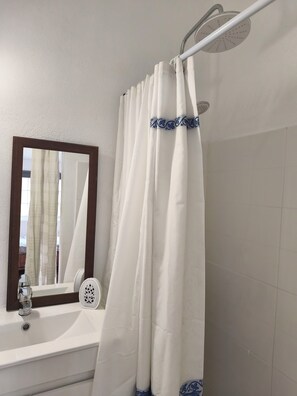 Ein Badezimmer mit einer weißen Badewanne, einer Duschvorhang mit blauer Borte, einem Spiegel und einem Wasserhahn.