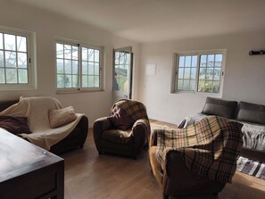 A living room with a sofa, armchair, and a wooden coffee table. There are large windows providing natural light. - Vrbo Property (Cartaxo)