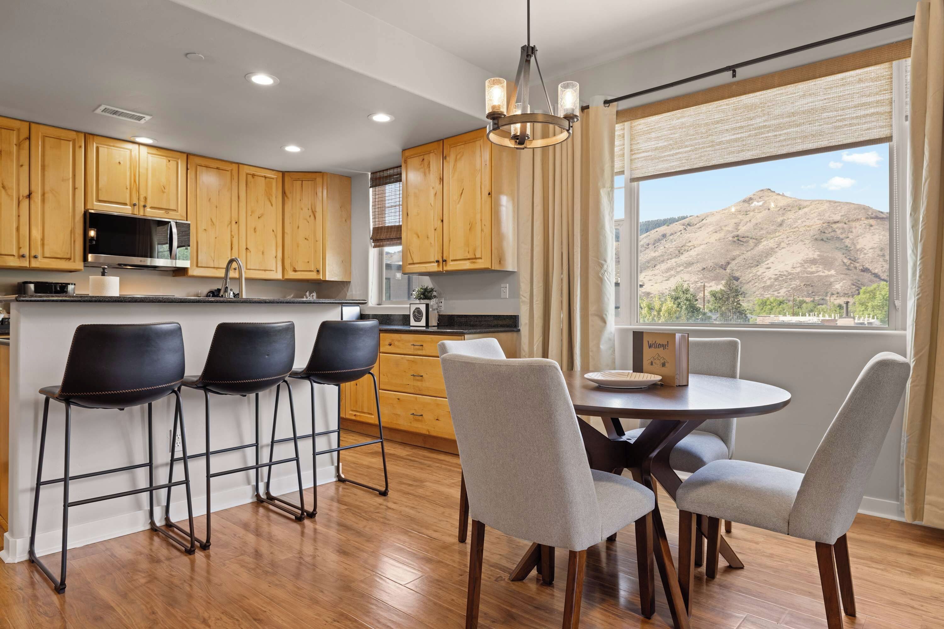 A modern kitchen with wooden cabinets, a built-in microwave, and a large window with a mountain view.