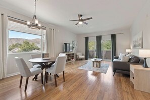 A spacious living room with a dining area, a ceiling fan, a TV, and a view of the outdoors.