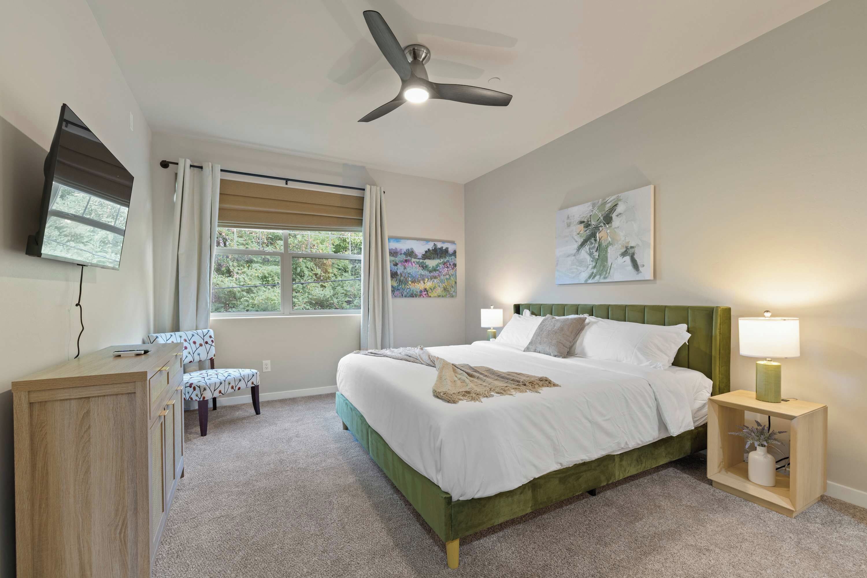 A bedroom with a bed, a desk, a chair, a ceiling fan, and a window with curtains.