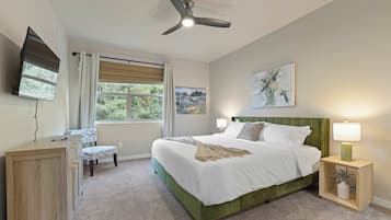 A bedroom with a bed, a desk, a chair, a ceiling fan, and a window with curtains.