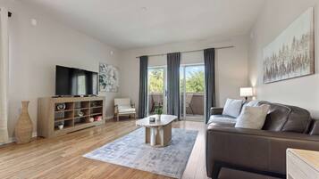 A modern living room with a flat-screen TV, a sofa, a coffee table, and a bookshelf.