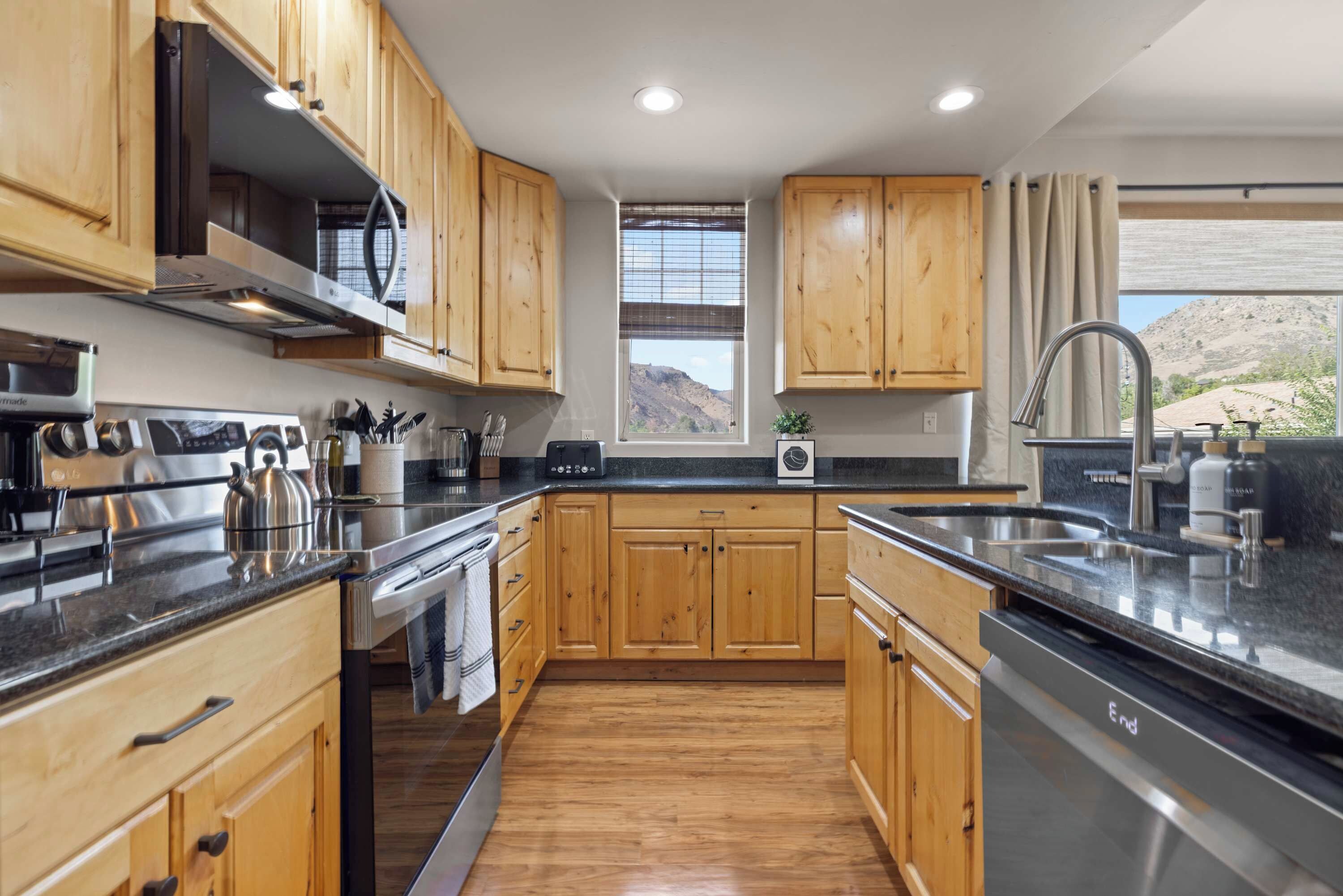 A modern kitchen with wooden cabinets, stainless steel appliances, and a view of a mountainous landscape.