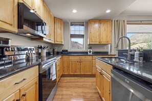 A modern kitchen with wooden cabinets, stainless steel appliances, and a view of a mountainous landscape.