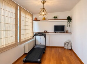 A compact room with a treadmill, a television, and a clock on the wall. - Nini's Maison - Terrace Living Above Kalamata City (Kalamata)