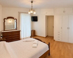 A bedroom with a bed, dresser, mirror, television, wardrobe, and a small table with a plant. - Nini's Maison - Terrace Living Above Kalamata City (Kalamata)