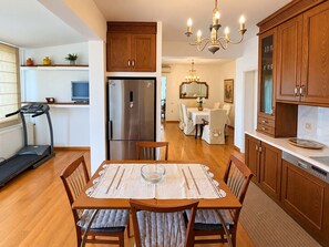 Een moderne keuken met houten kastjes, een roestvrijstalen koelkast, een eettafel met stoelen, en een loopband in de aangrenzende kamer.