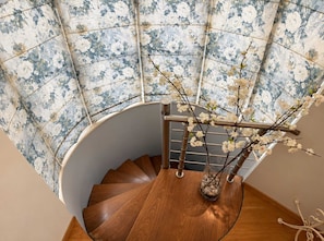 Een houten spiraaltrap met een wand in bloemenmotief en een vaas met takken.