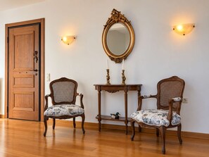 A room with two wooden chairs with floral upholstery, a wooden table, a mirror with an ornate frame, and a wooden door. - Nini's Maison - Terrace Living Above Kalamata City (Kalamata)