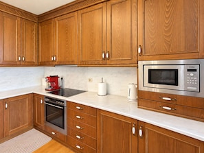 A kitchen with wooden cabinets, a stainless steel microwave, a red coffee maker, and a built-in oven. - Nini's Maison - Terrace Living Above Kalamata City (Kalamata)