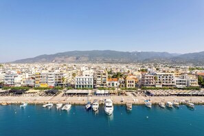 A coastal cityscape with a marina filled with boats, surrounded by residential buildings and mountains in the background. - Nini's Maison - Terrace Living Above Kalamata City (Kalamata)