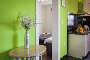 A modern kitchen with a green wall, a small round table with a vase of flowers, and a fruit bowl on the counter. - A1 - Modern apartment with big garden and terrace with sea view, 80m from beach (Vinišće)