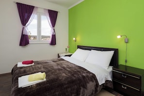 Een hotelkamer met een bed, nachtkastje, lamp en raam met paarse gordijnen.