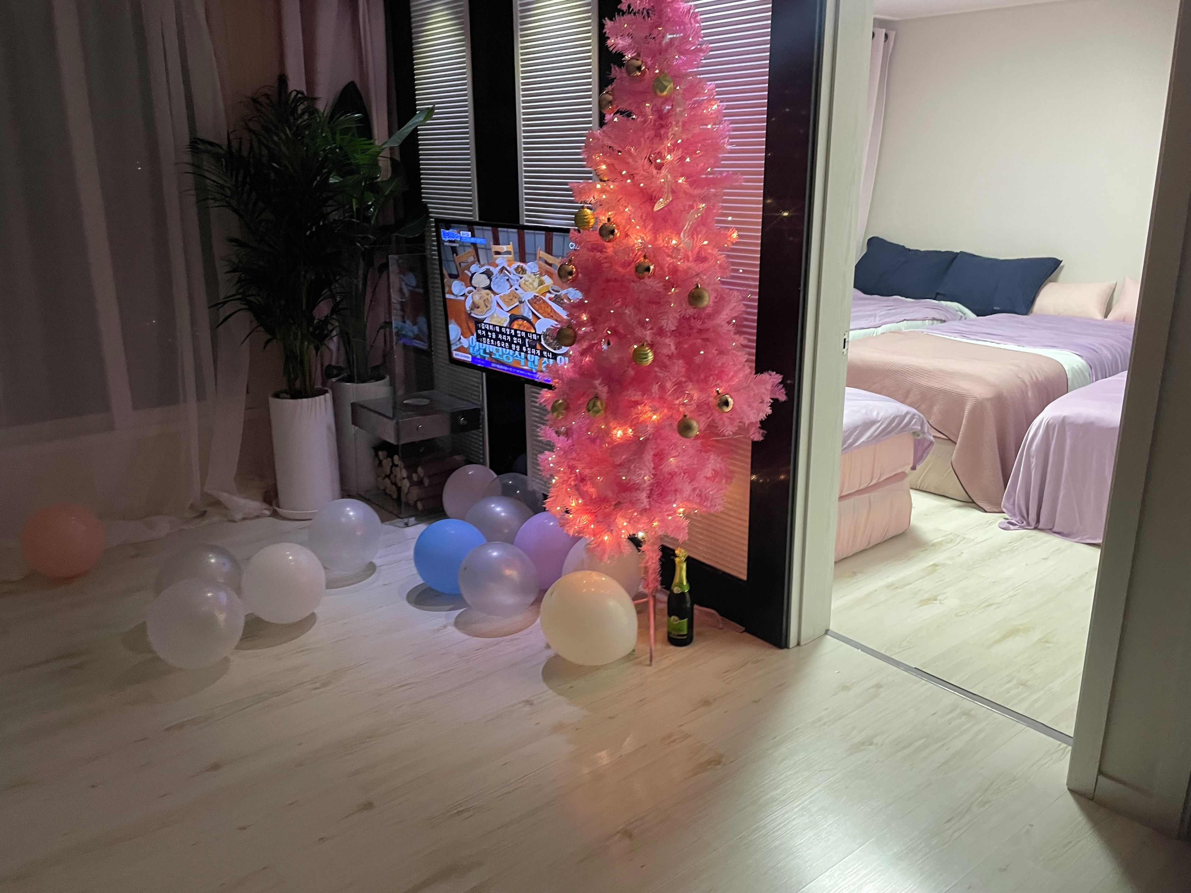 A room with a pink artificial tree, a television, and a bed with a blue pillow.