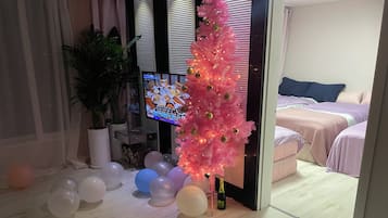 A room with a pink artificial tree, a television, and a bed with a blue pillow.