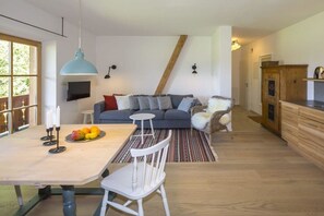 A modern living space with a dining area, a sofa set, a television mounted on the wall, and a kitchen area with wooden cabinets. - Mayrhof West Apartment (Mittenwald)