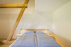 Ett rum med ett sluttande tak, två sängar med rutigt sänglinne, två sänglampor och ett litet bord.