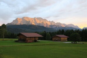 Un paysage rural avec deux granges en bois et une chaîne de montagnes en arrière-plan.