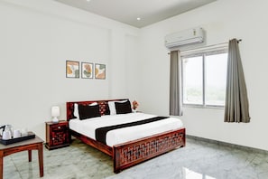 A hotel room with a bed, bedside table, lamp, air conditioning unit, window with curtains, and wall art. - Hotel College And Institute Technology (Jalsu)