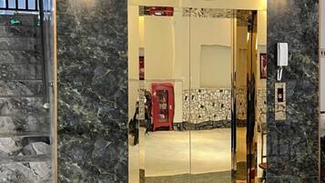 A hotel entrance with a marble wall, a glass door, and a red carpet leading inside.