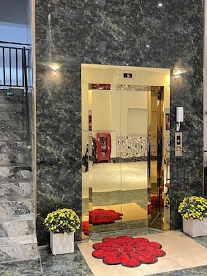 L’entrée d’un hôtel, avec un mur de marbre, une porte en verre et un tapis rouge qui mène à l’intérieur.