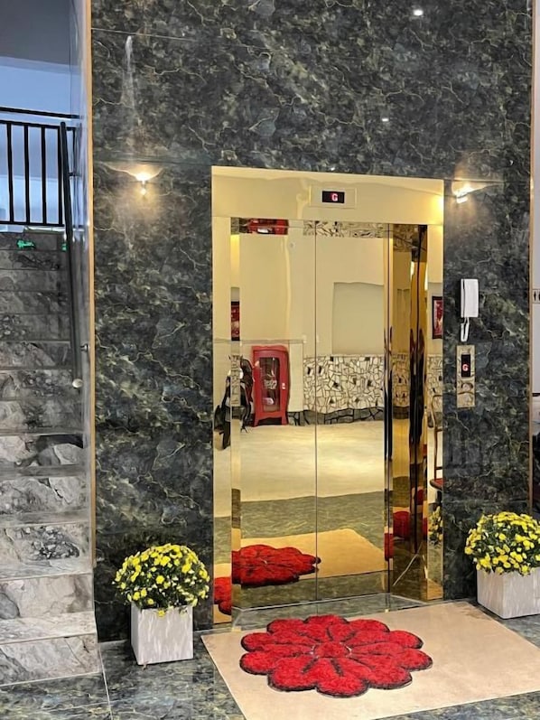 A hotel entrance with a marble wall, a glass door, and a red carpet leading inside.