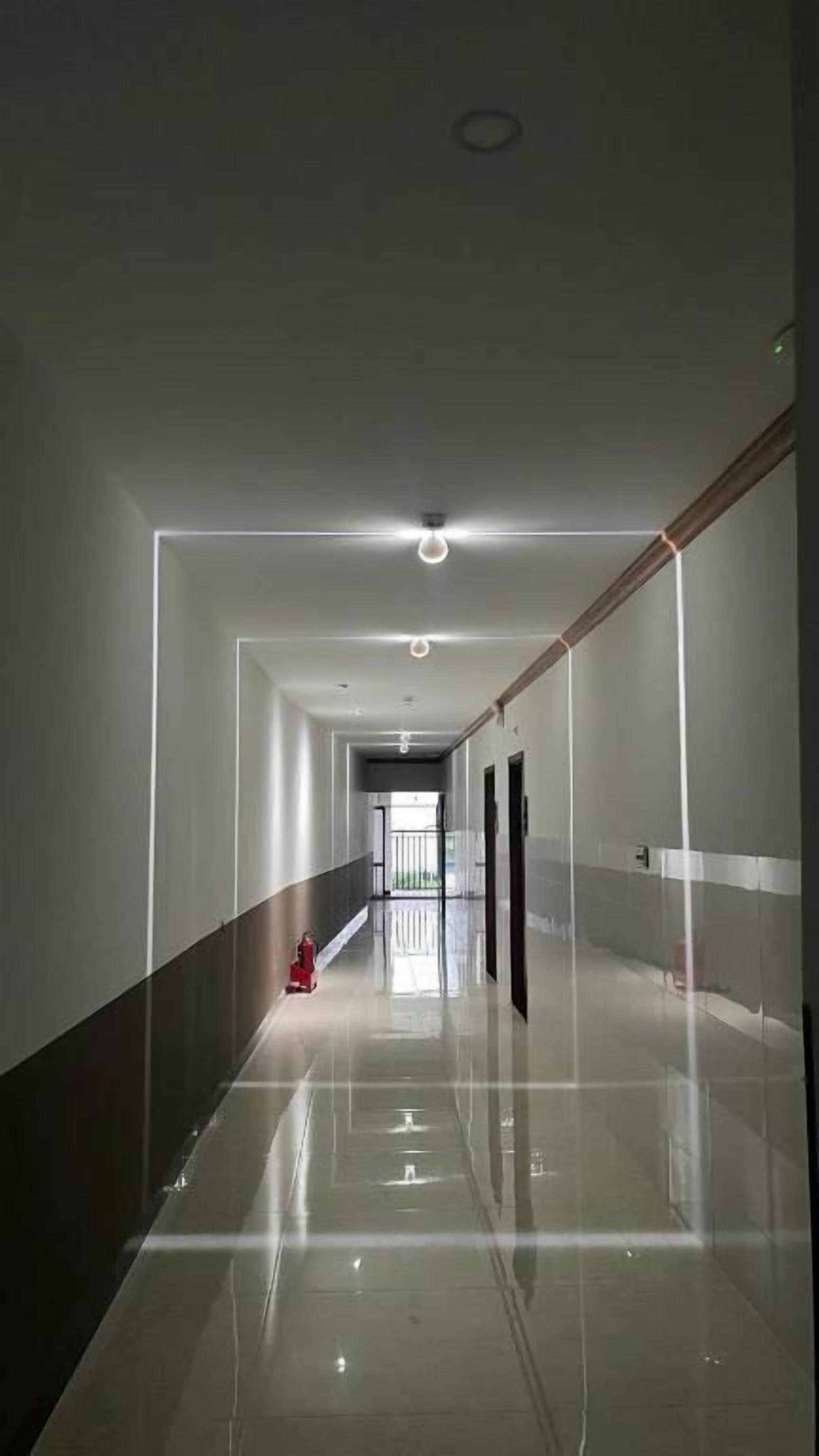 Un pasillo largo y estrecho con piso brillante, un extintor y una puerta al final.