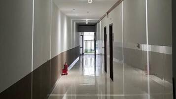 Un pasillo largo y estrecho con piso brillante, un extintor y una puerta al final.