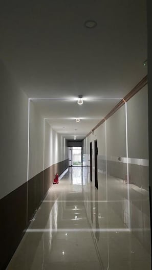 A long, narrow hallway with a shiny floor, a fire extinguisher, and a door at the end.