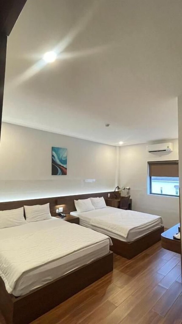 Une chambre d’hôtel avec deux lits, une table de chevet, une commode, un climatiseur fixé au mur et une fenêtre.