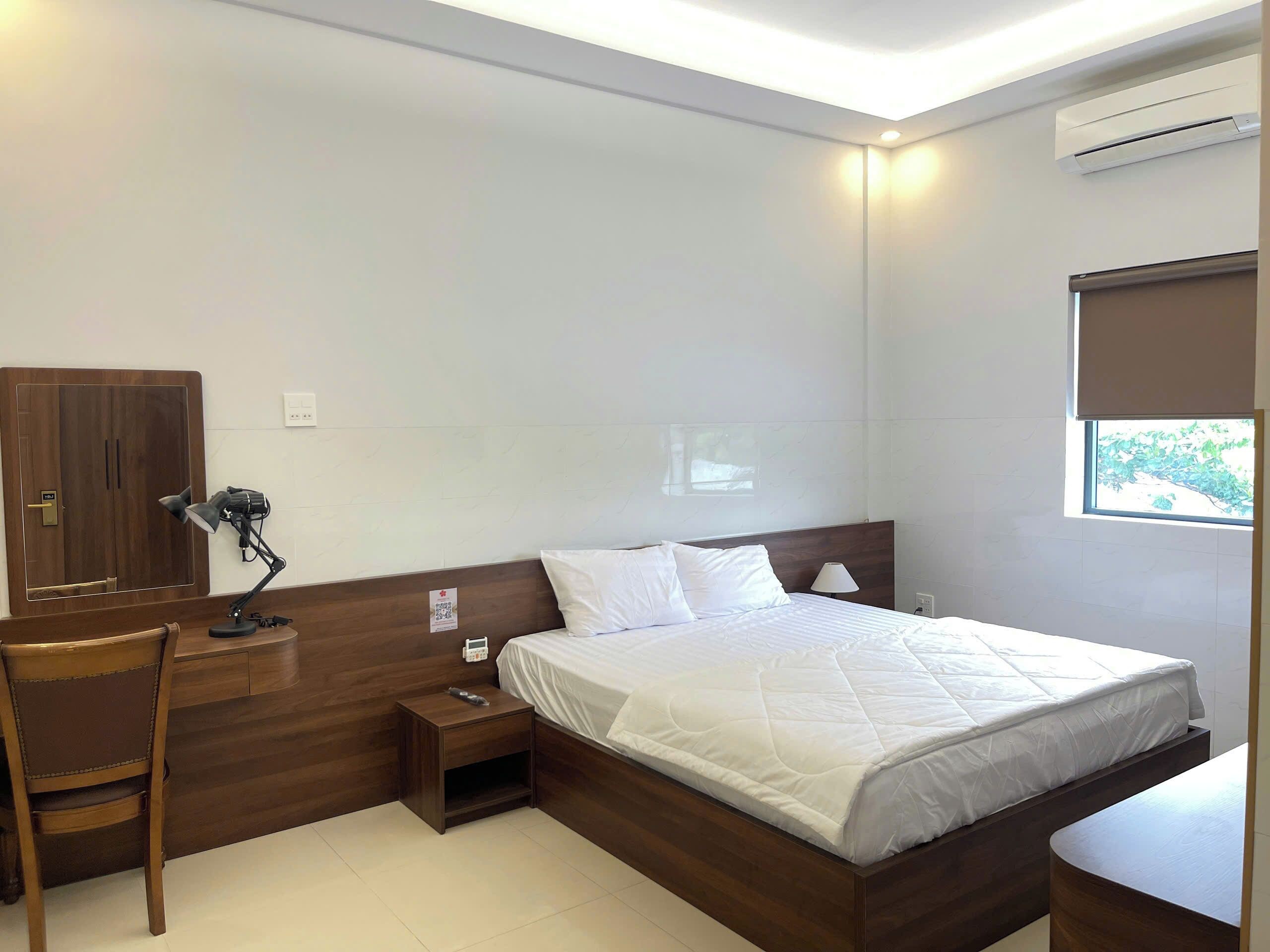 Habitación de hotel con cama, escritorio, silla, mesita de noche y aire acondicionado.