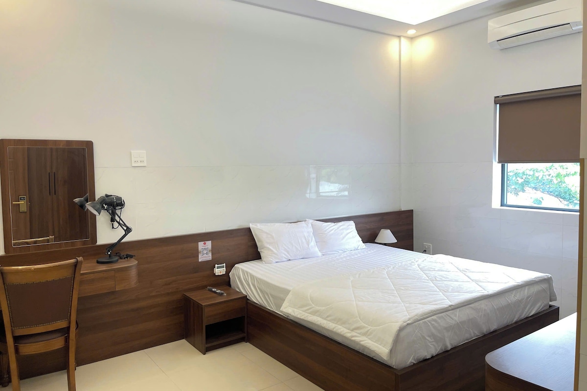 Habitación de hotel con cama, escritorio, silla, mesita de noche y aire acondicionado.
