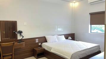Habitación de hotel con cama, escritorio, silla, mesita de noche y aire acondicionado.